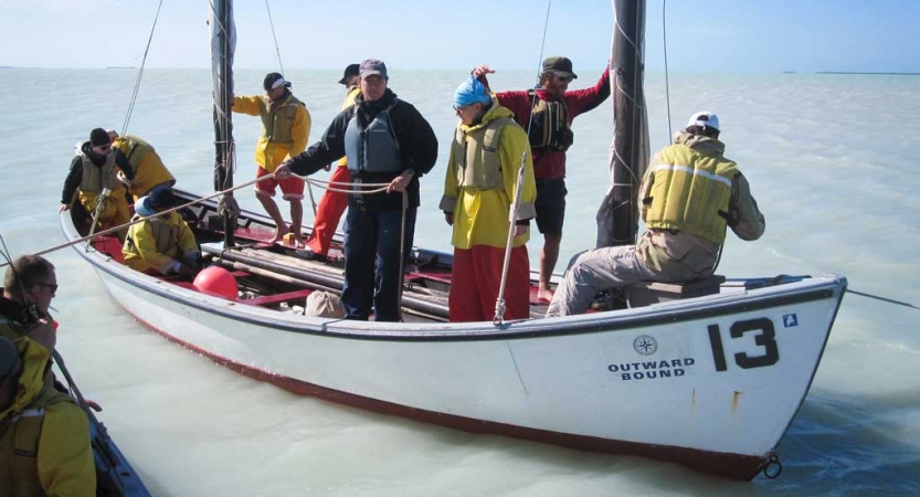 A group of people wearing life jackets practice sailing techniques on an outward bound expedition 
